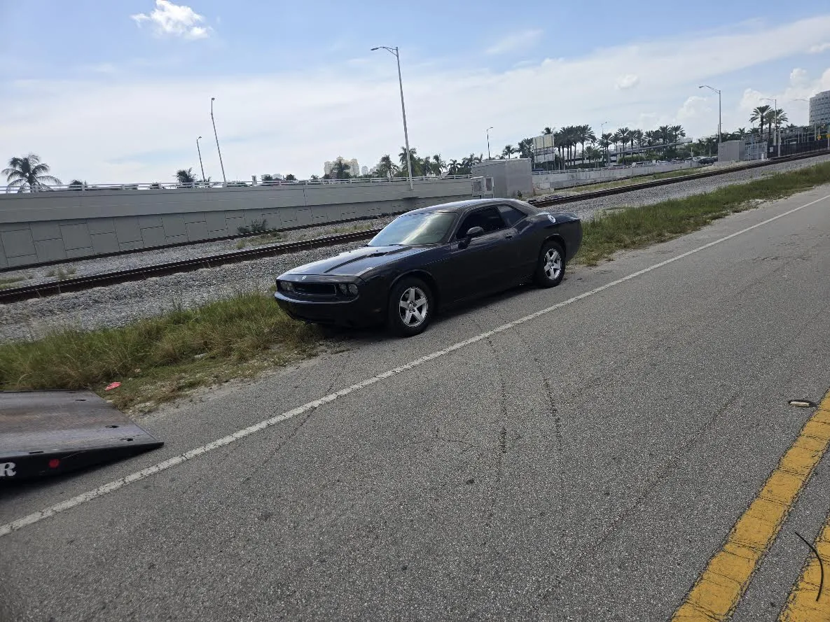 Real dark Dodge Challenger near a flatbed truck as a vehicle pickup example for Miami Beach